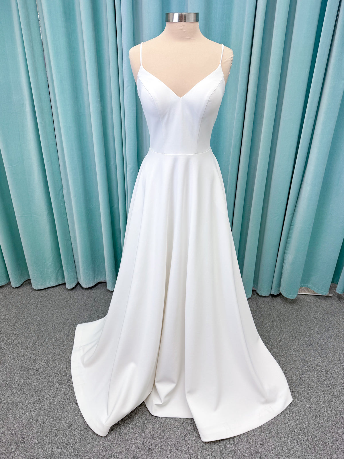 Minimalist crepe A-line wedding dress with spaghetti straps, V-neckline, fitted bodice, natural waist, and flowing skirt.