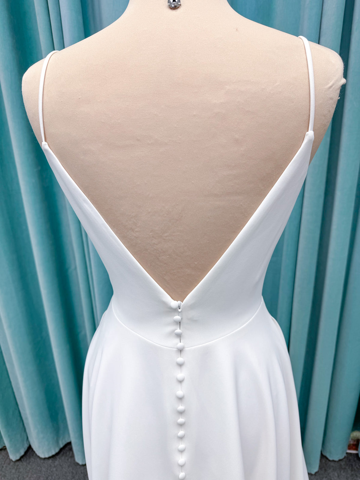 Minimalist crepe A-line wedding dress with spaghetti straps, V-neckline, fitted bodice, natural waist, and flowing skirt.