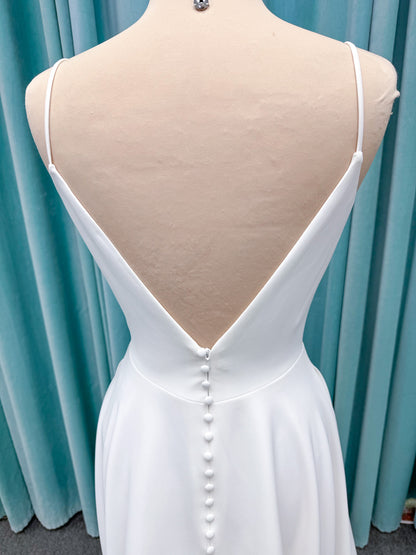 Minimalist crepe A-line wedding dress with spaghetti straps, V-neckline, fitted bodice, natural waist, and flowing skirt.