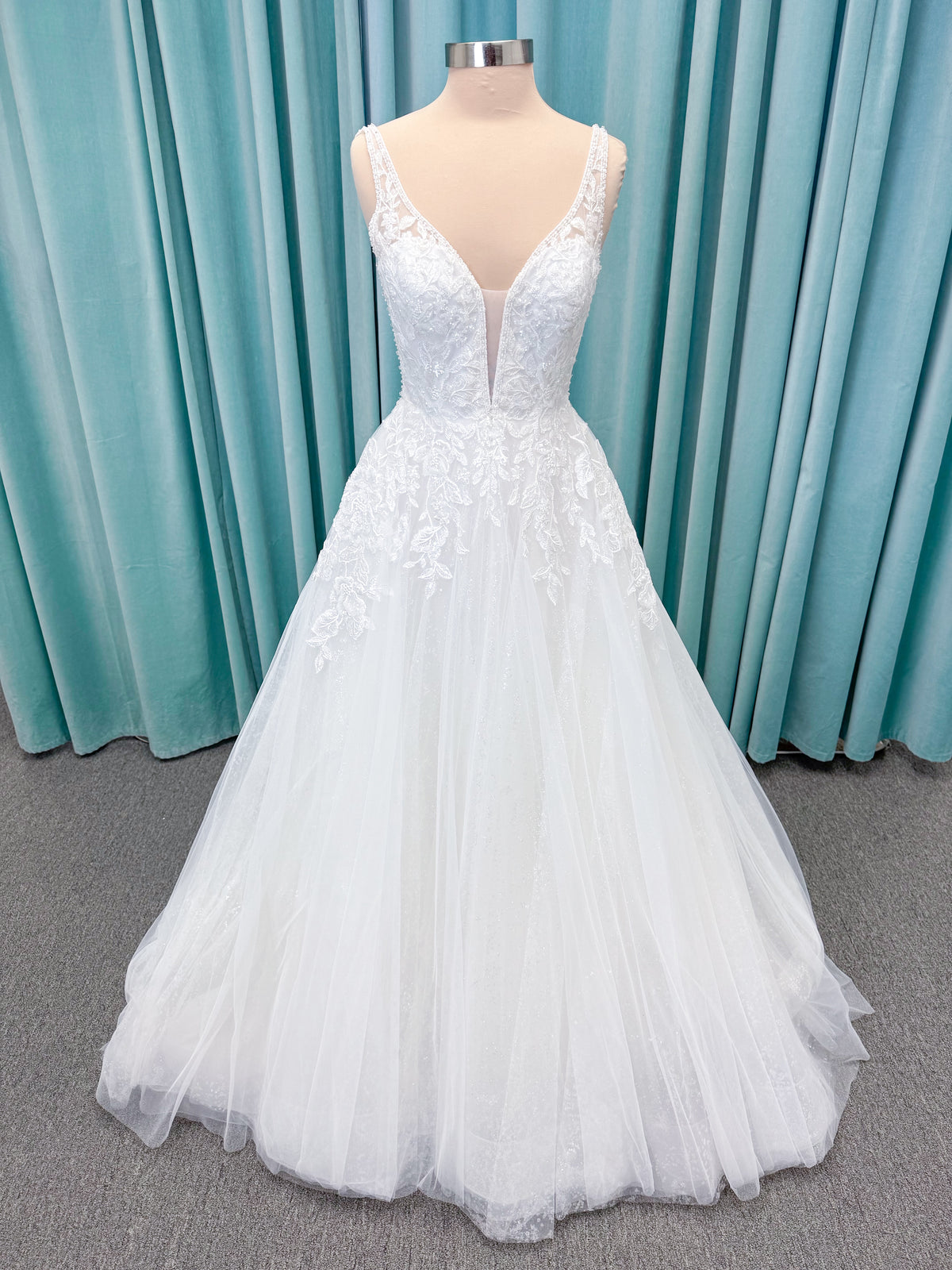 Morilee 1010021 Myrtha A-line wedding dress on mannequin with plunging V-neckline, sheer low scoop back, and glitter tulle lace applique