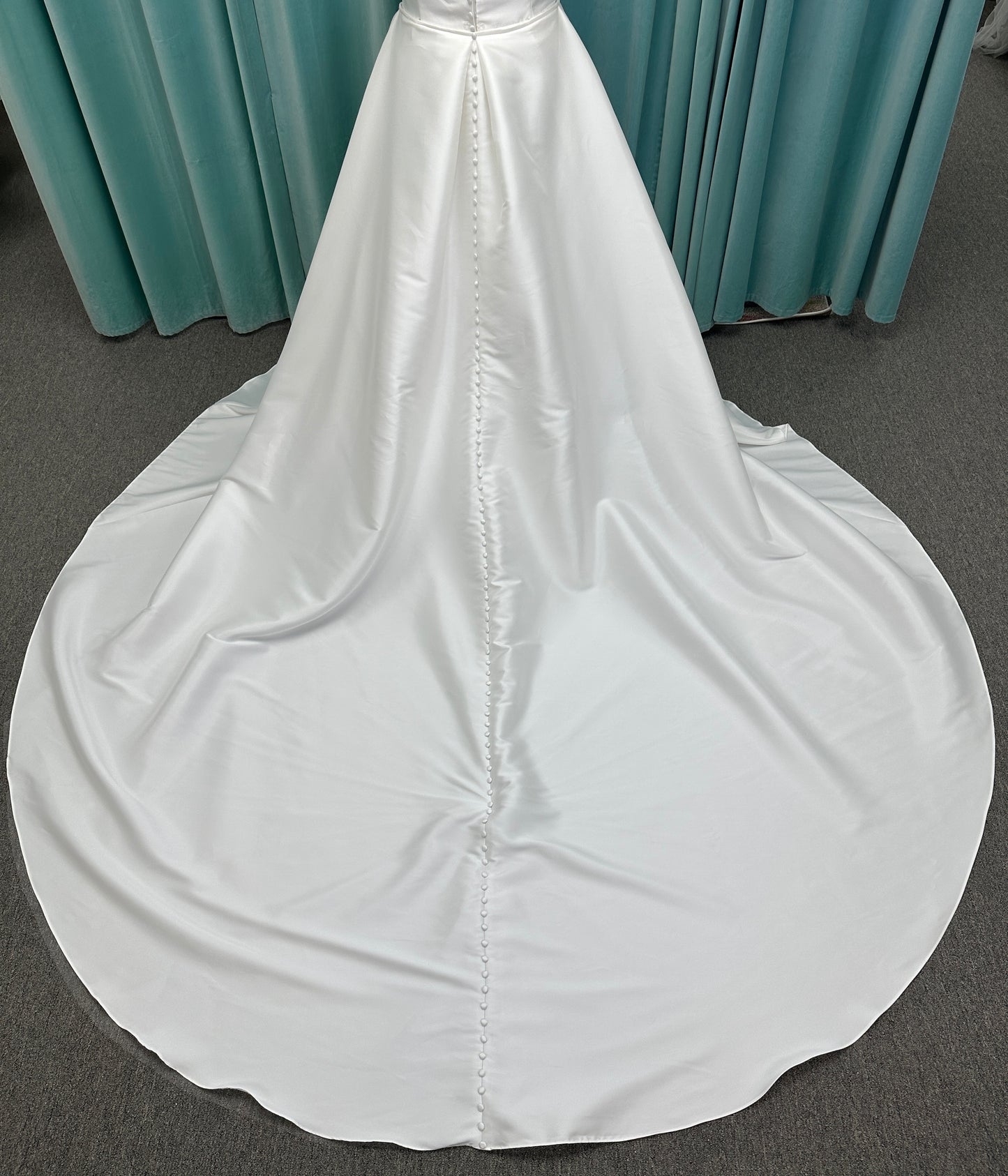 Oh Darling ivory strapless satin sheath wedding dress on mannequin with bandeau neckline, oversized statement bow at the waist, and voluminous overskirt.
