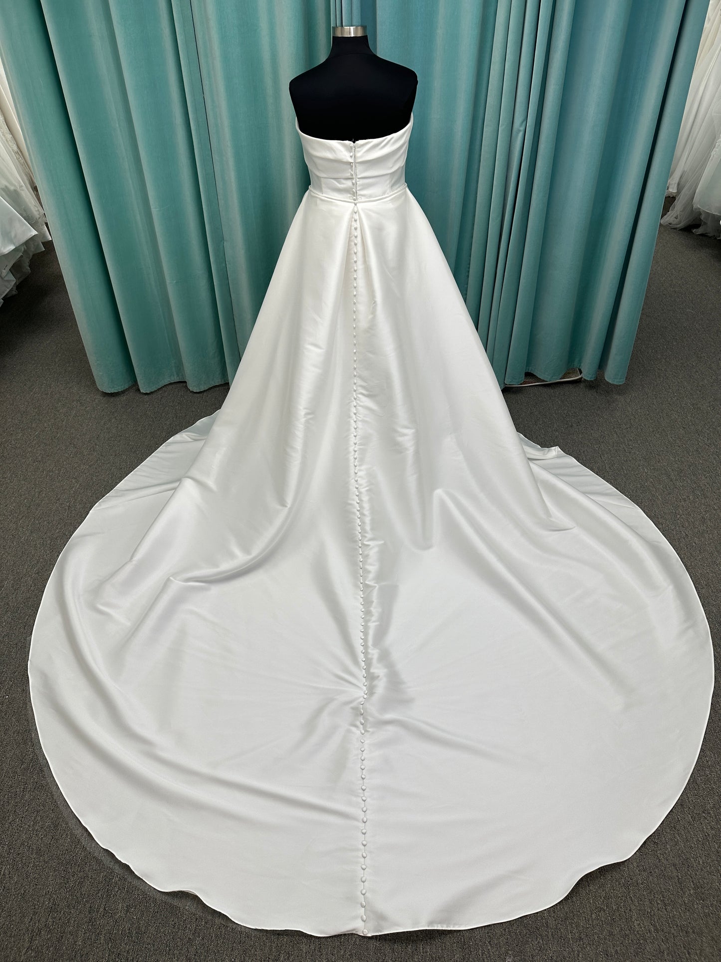 Oh Darling ivory strapless satin sheath wedding dress on mannequin with bandeau neckline, oversized statement bow at the waist, and voluminous overskirt.
