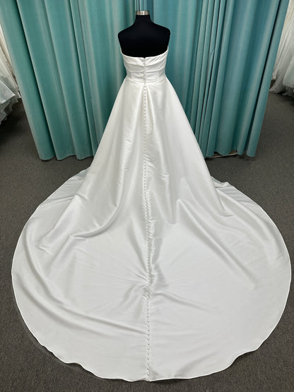 Oh Darling ivory strapless satin sheath wedding dress on mannequin with bandeau neckline, oversized statement bow at the waist, and voluminous overskirt.
