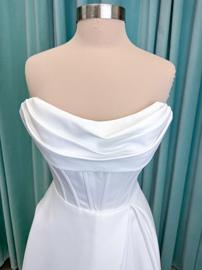 Morilee 15054 Pippa A-line wedding dress on mannequin with cowl neckline, corset bodice, petal satin skirt slit, and pockets