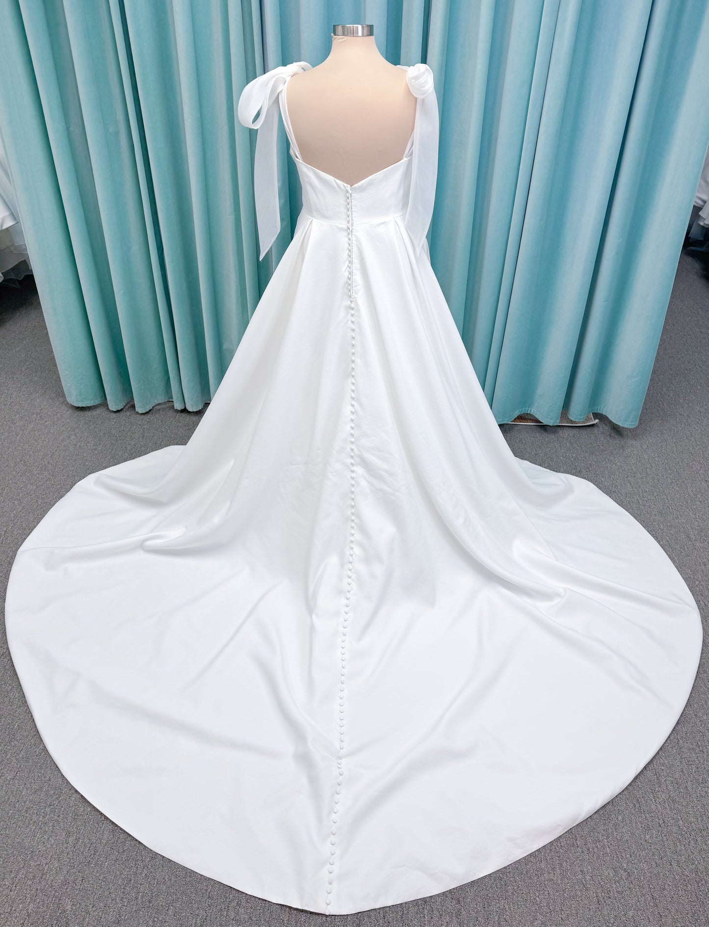 Morilee 4473 Reba plus size A-line wedding dress in Larissa satin with cowl strapless neck, detachable organza bow tie straps, and covered buttons to hem.