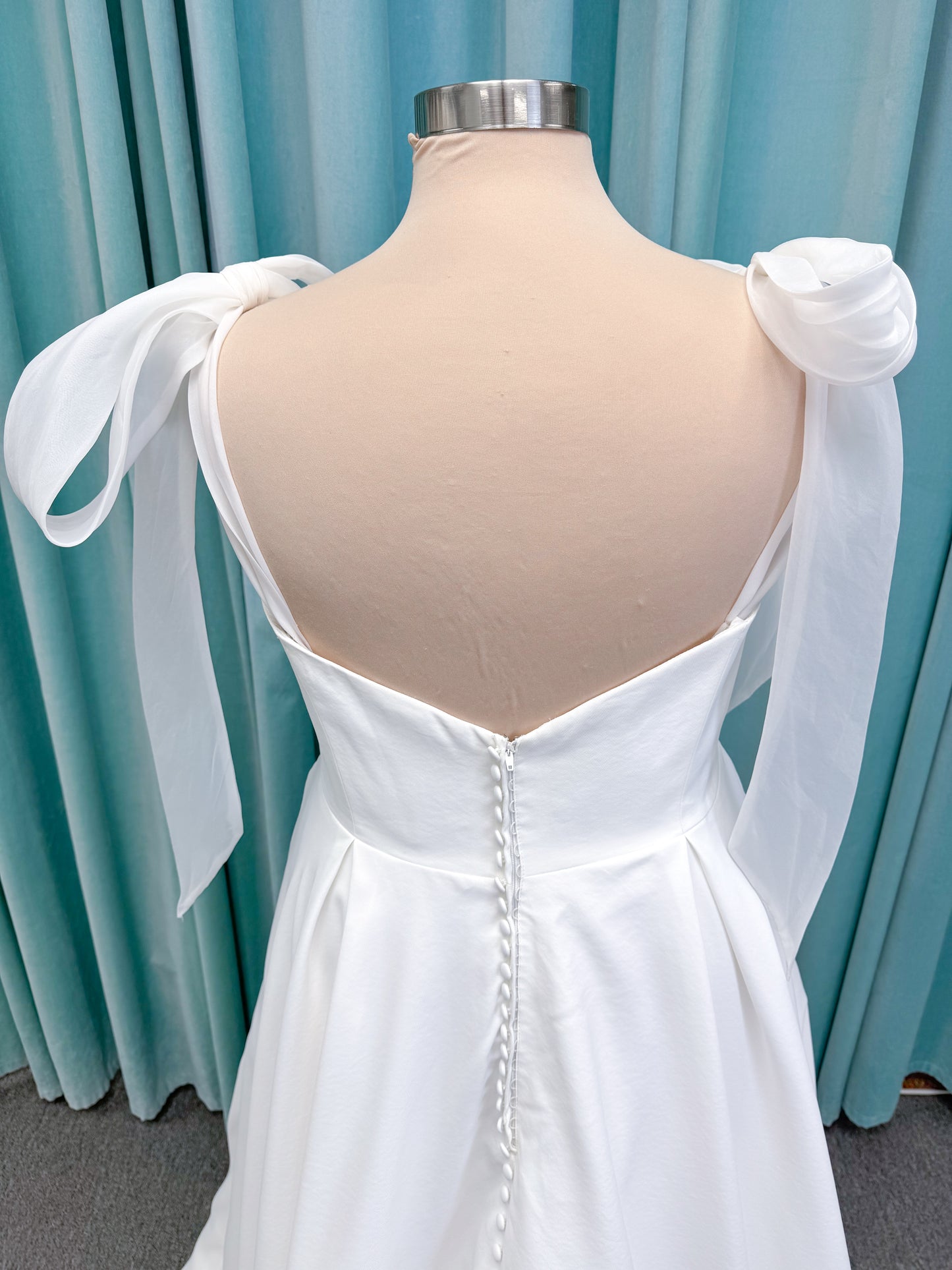 Morilee 4473 Reba plus size A-line wedding dress in Larissa satin with cowl strapless neck, detachable organza bow tie straps, and covered buttons to hem.