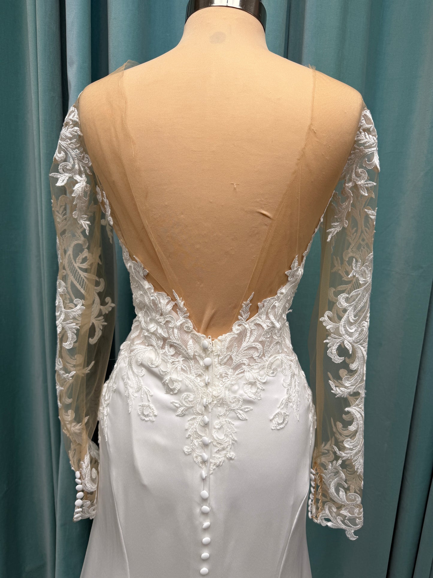Stella York 8028 ivory lace fit-and-flare wedding dress on mannequin featuring high illusion neckline, sheer long lace sleeves, plunging bodice, and low open back.
