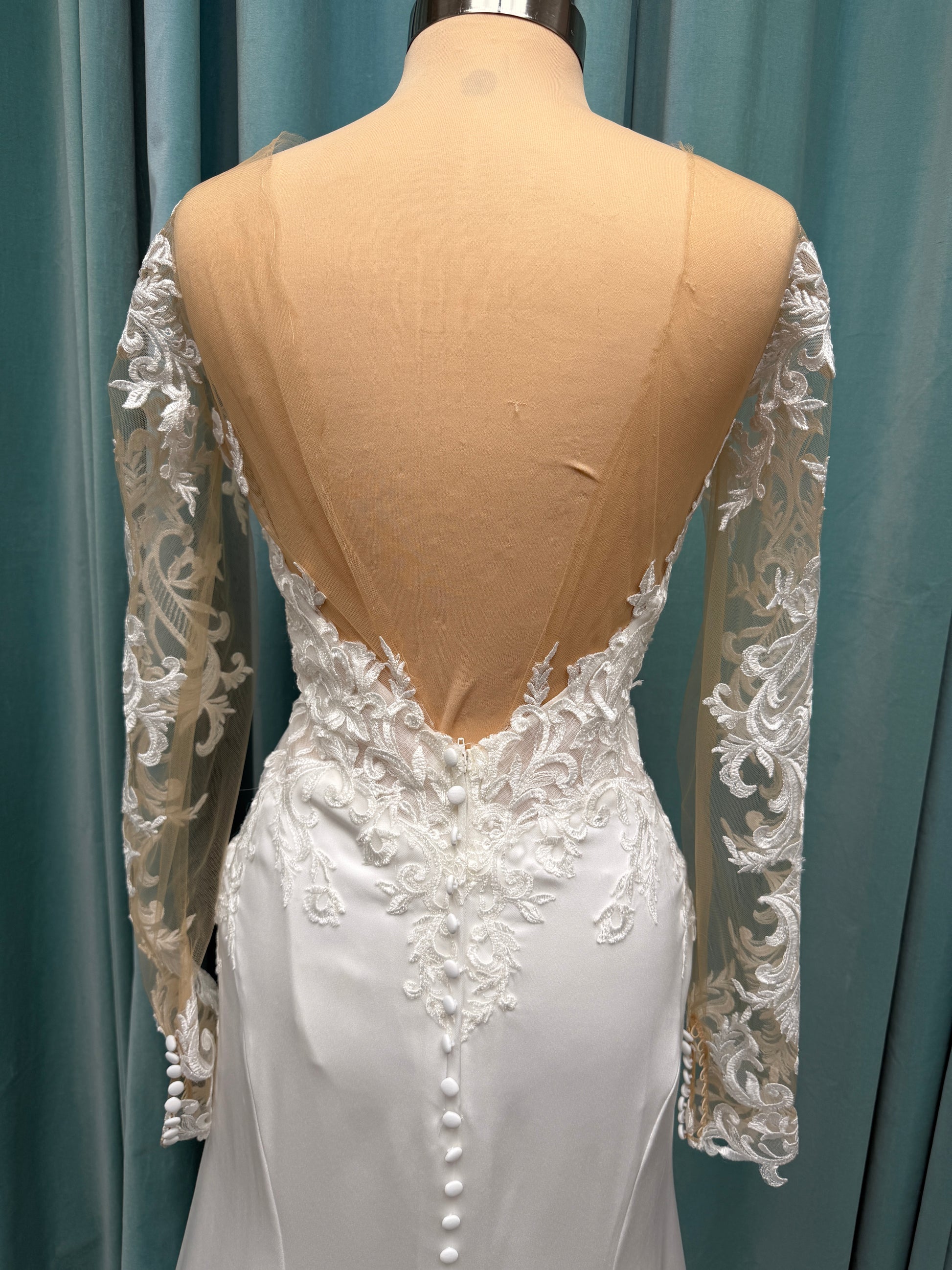 Stella York 8028 ivory lace fit-and-flare wedding dress on mannequin featuring high illusion neckline, sheer long lace sleeves, plunging bodice, and low open back.
