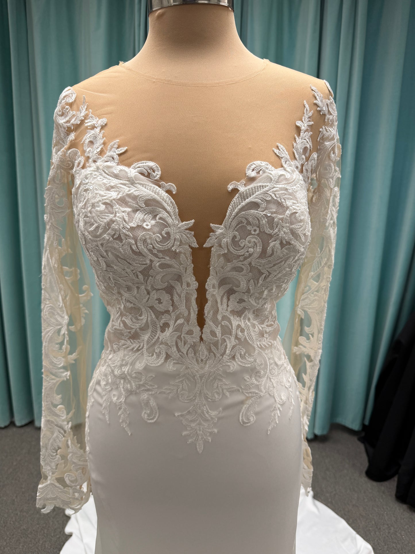 Stella York 8028 ivory lace fit-and-flare wedding dress on mannequin featuring high illusion neckline, sheer long lace sleeves, plunging bodice, and low open back.
