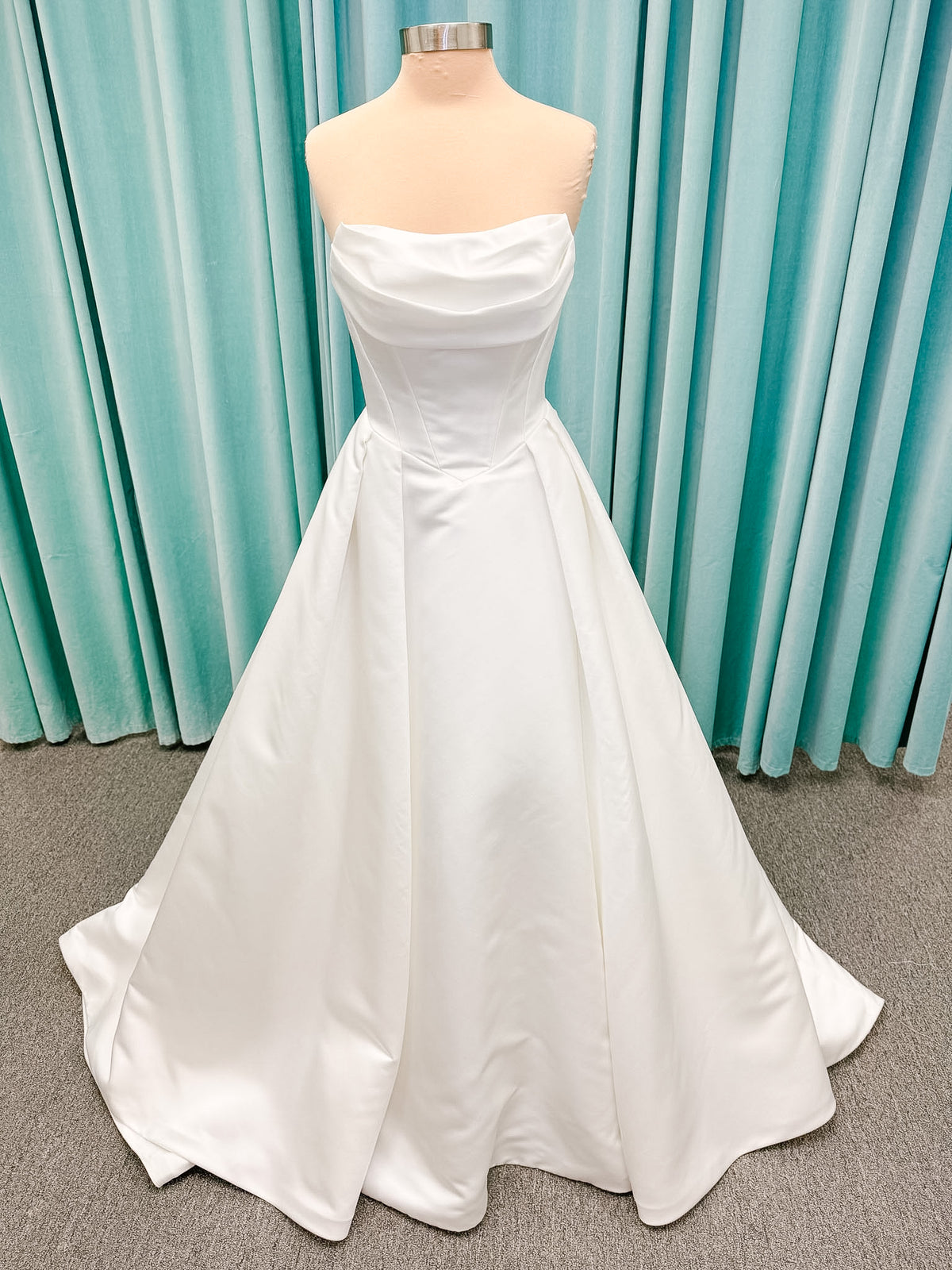 Stella York SY8084 ballgown wedding dress on mannequin with strapless ruched neckline, basque waist bodice, pleated satin skirt, and row of fabric-covered buttons