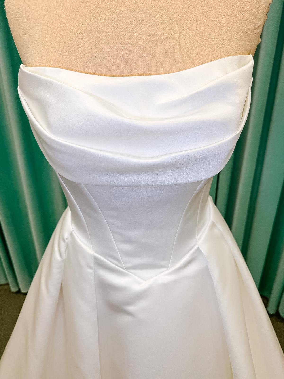 Stella York SY8084 ballgown wedding dress on mannequin with strapless ruched neckline, basque waist bodice, pleated satin skirt, and row of fabric-covered buttons