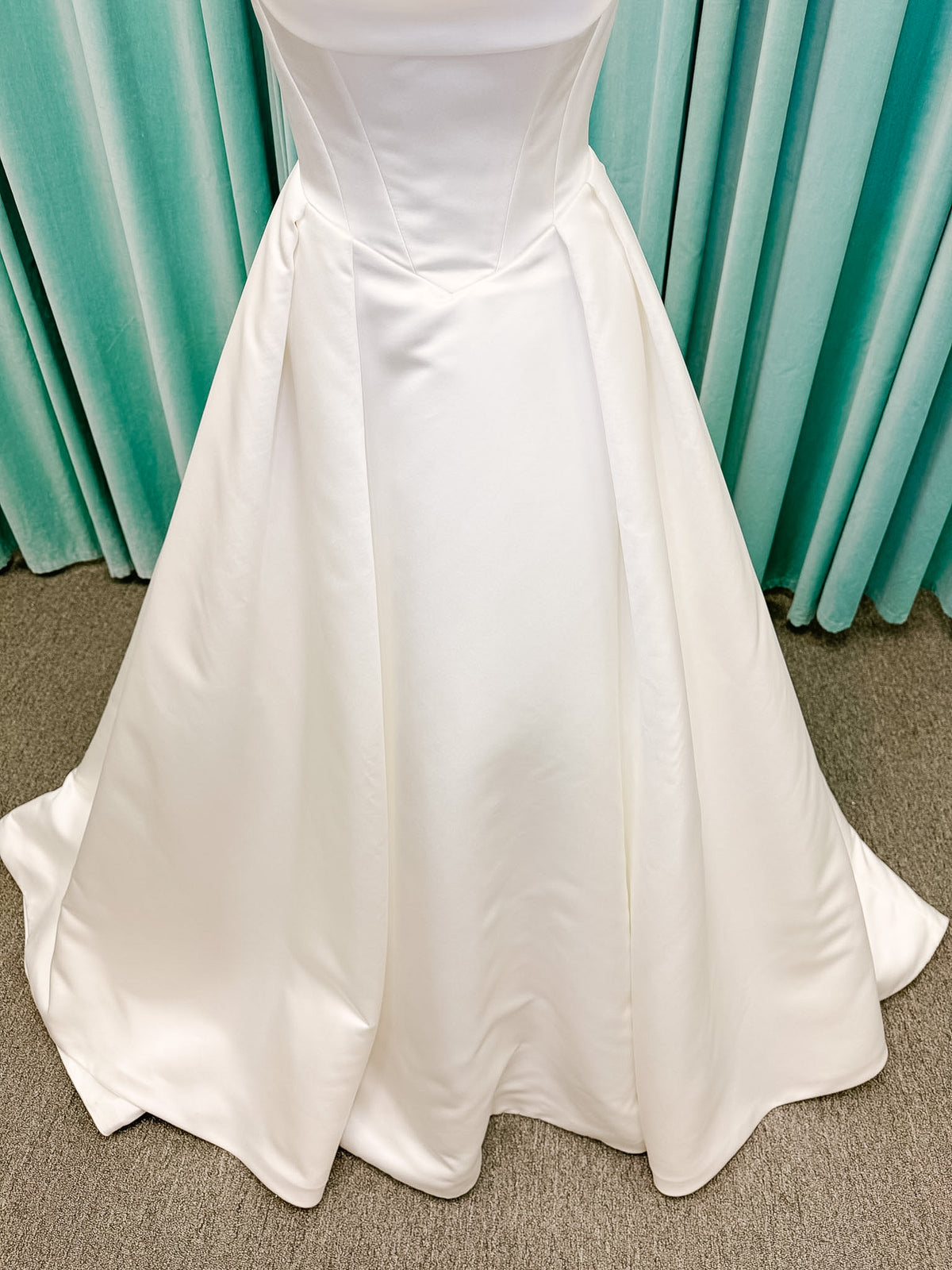 Stella York SY8084 ballgown wedding dress on mannequin with strapless ruched neckline, basque waist bodice, pleated satin skirt, and row of fabric-covered buttons