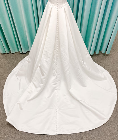 Stella York SY8084 ballgown wedding dress on mannequin with strapless ruched neckline, basque waist bodice, pleated satin skirt, and row of fabric-covered buttons