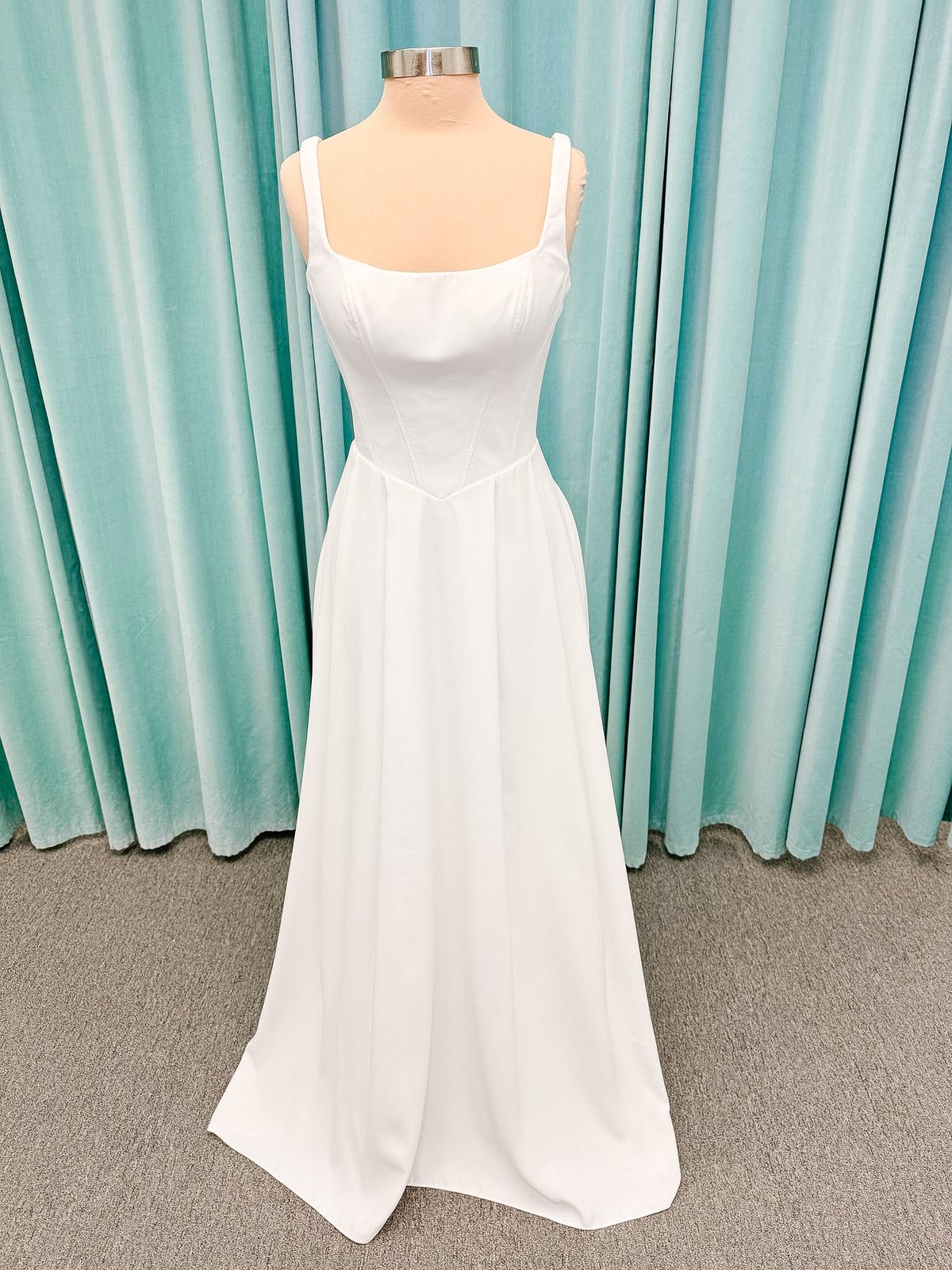 Stella York SY8180 A-line wedding dress on mannequin with wide straps, square neckline, contoured matte satin bodice, angled waist, and soft A-line skirt