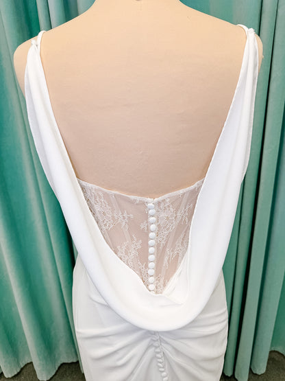 Stella York SY8224 sheath wedding dress on mannequin with spaghetti straps, draped scoop neckline, ruched crepe bodice, front slit, and detachable back cowl