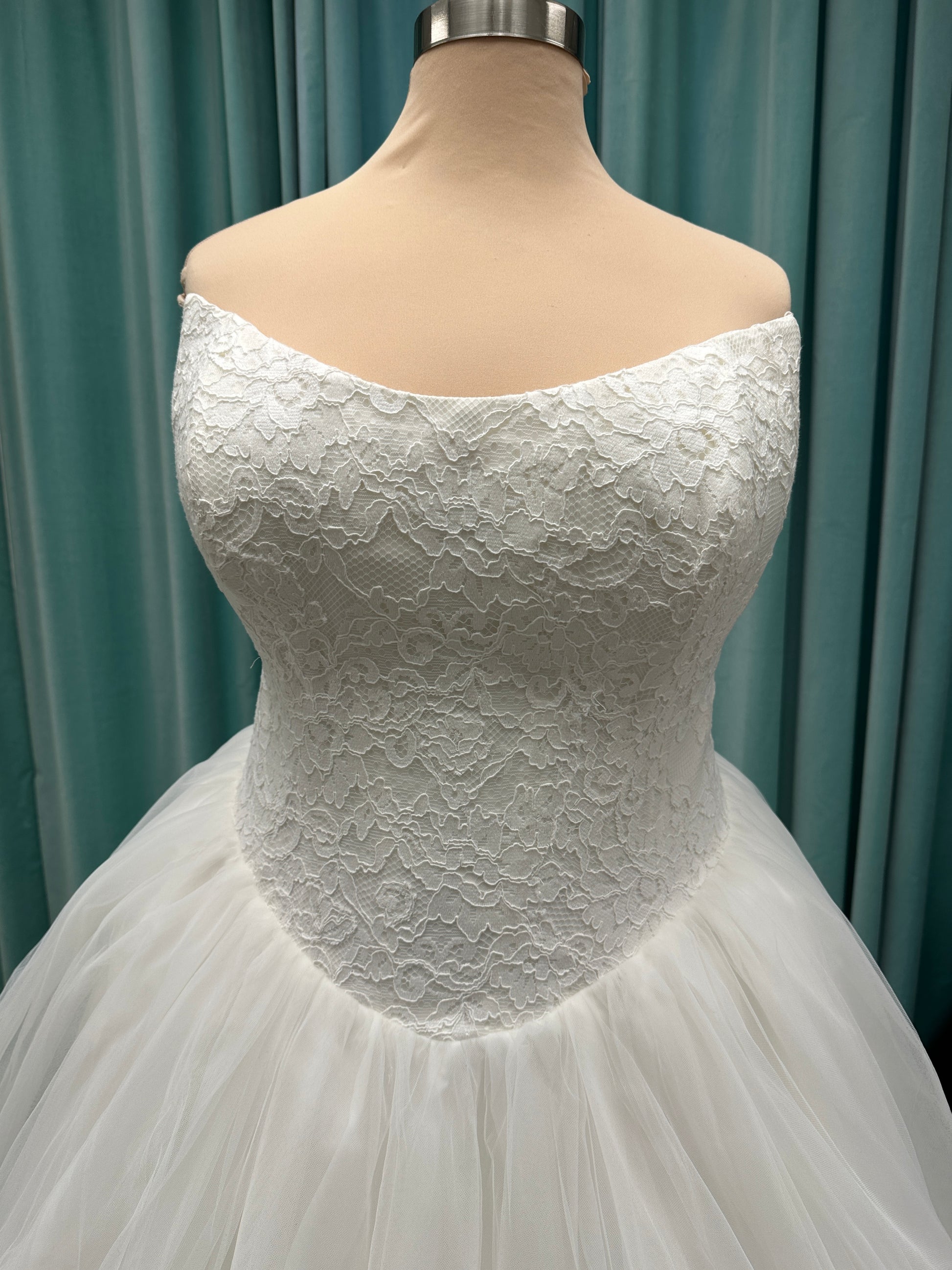 Plus size strapless lace ballgown wedding dress with cat-eye neckline, basque waist, full tulle skirt, and detachable satin bow by Stella York Style SY8189