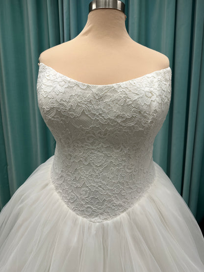Plus size strapless lace ballgown wedding dress with cat-eye neckline, basque waist, full tulle skirt, and detachable satin bow by Stella York Style SY8189