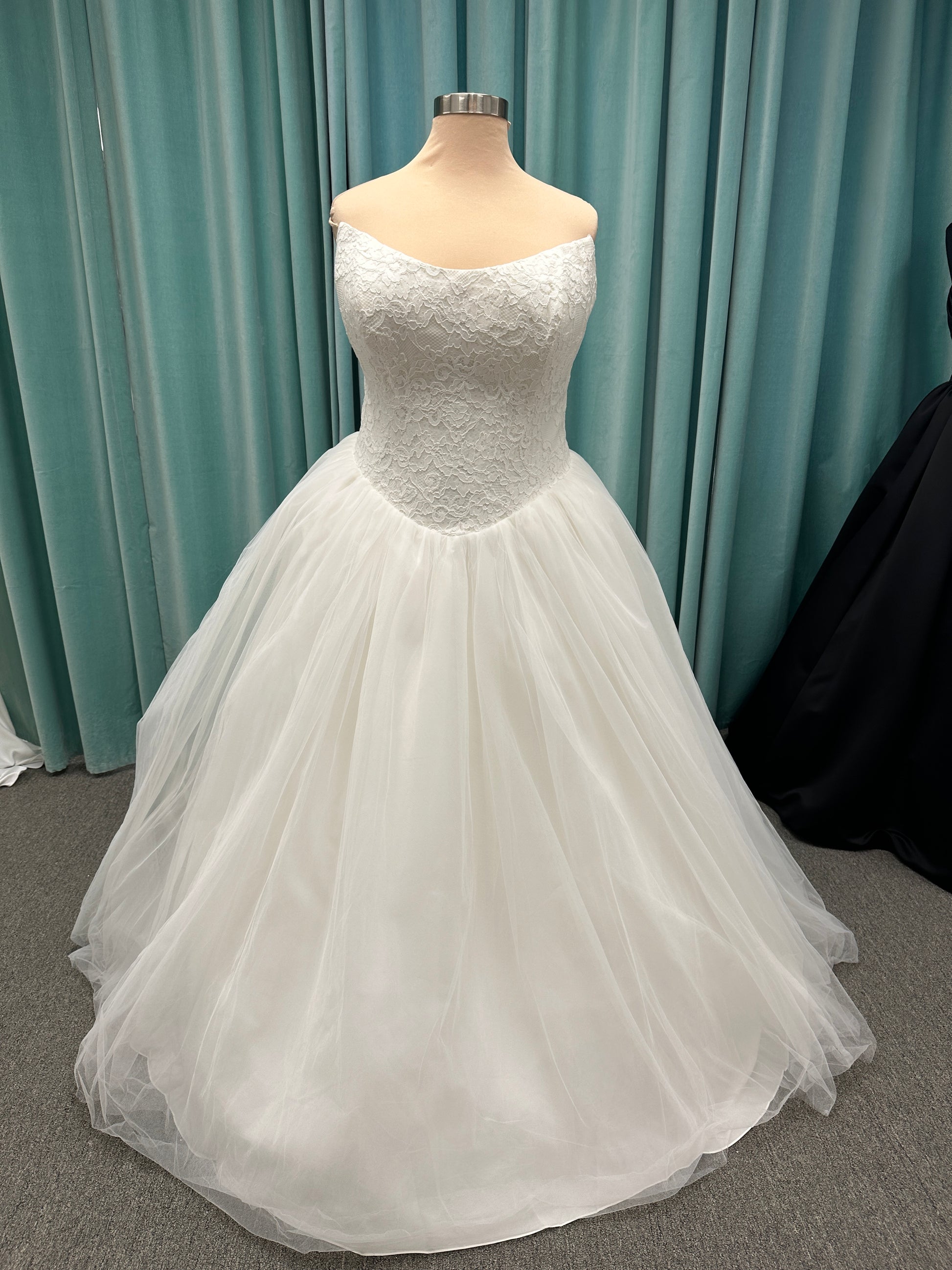 Plus size strapless lace ballgown wedding dress with cat-eye neckline, basque waist, full tulle skirt, and detachable satin bow by Stella York Style SY8189