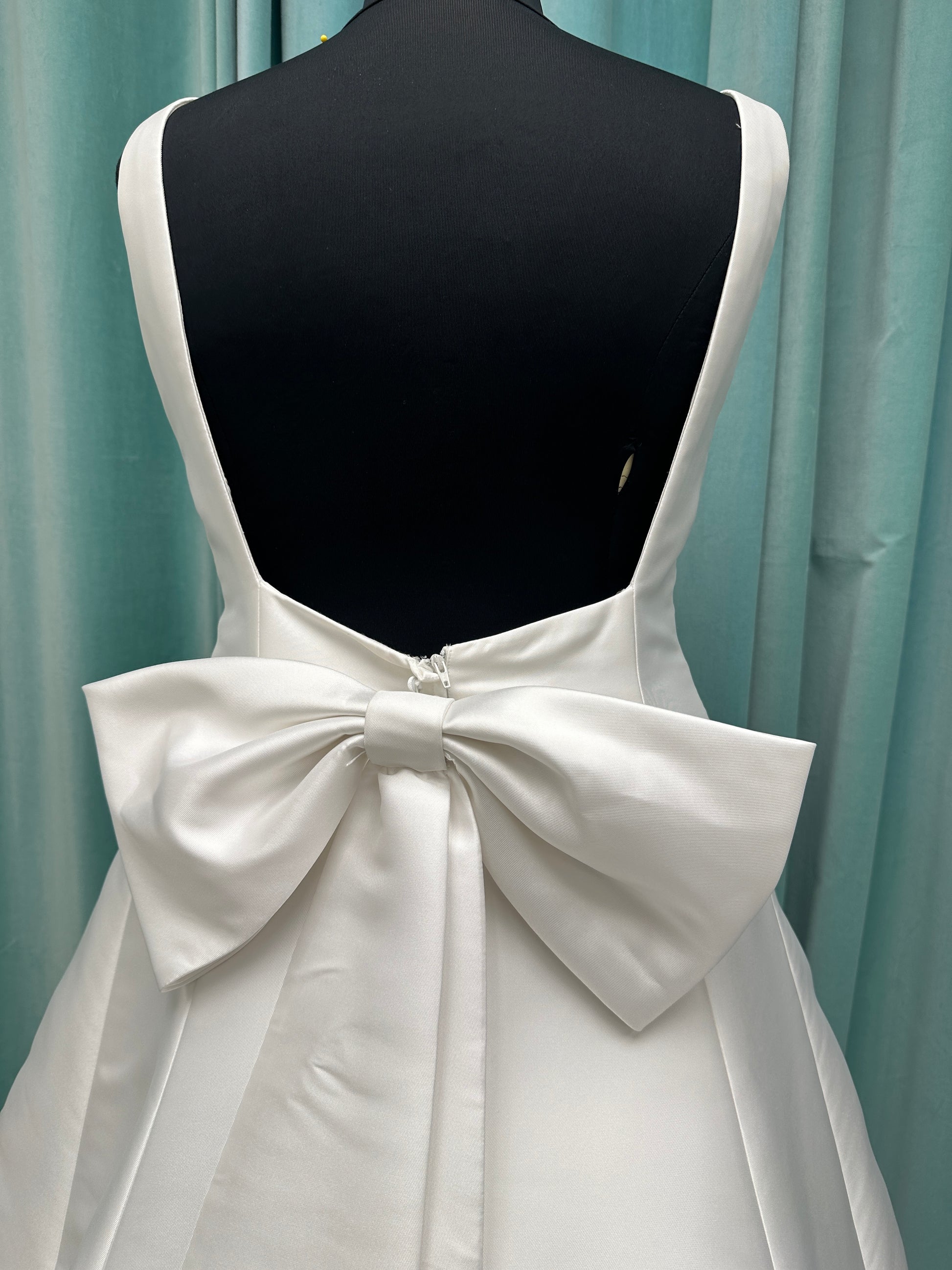 Minimalist Mikado A-line wedding dress with square neckline, clean seams, subtle side cutouts, and detachable oversized bow at the back