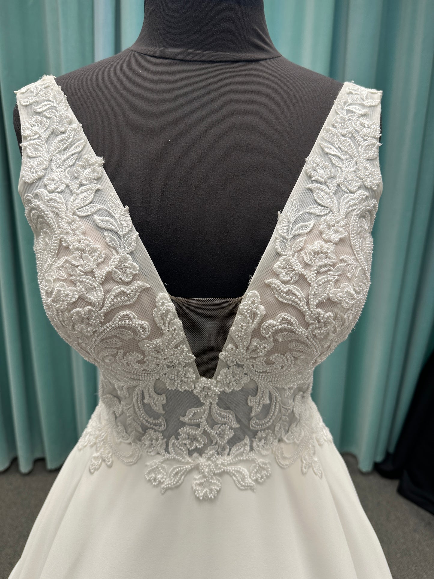 Satin A-line wedding dress with deep V-neckline, lace bodice, illusion tulle inset, and flowing skirt with pockets and long train