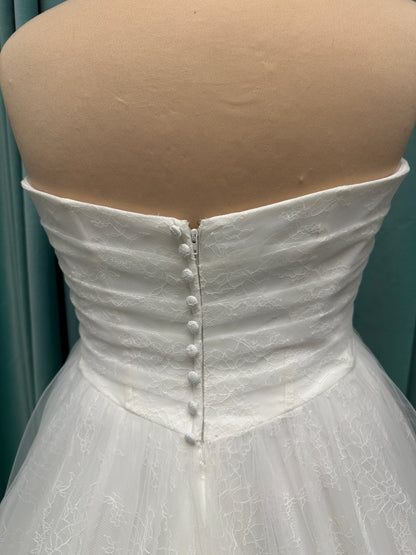 Plus size strapless A-line wedding dress with ruched tulle bodice, Chantilly lace detailing, basque waist, and flowing tulle skirt with train