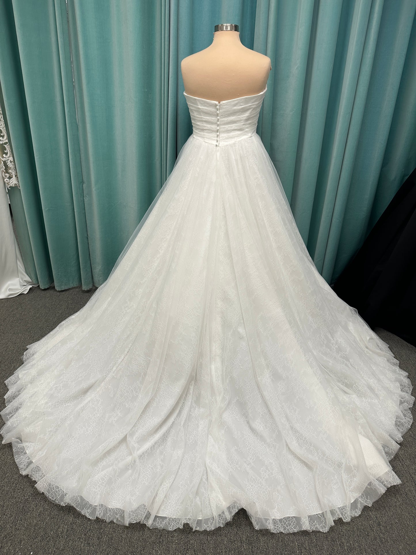 Plus size strapless A-line wedding dress with ruched tulle bodice, Chantilly lace detailing, basque waist, and flowing tulle skirt with train