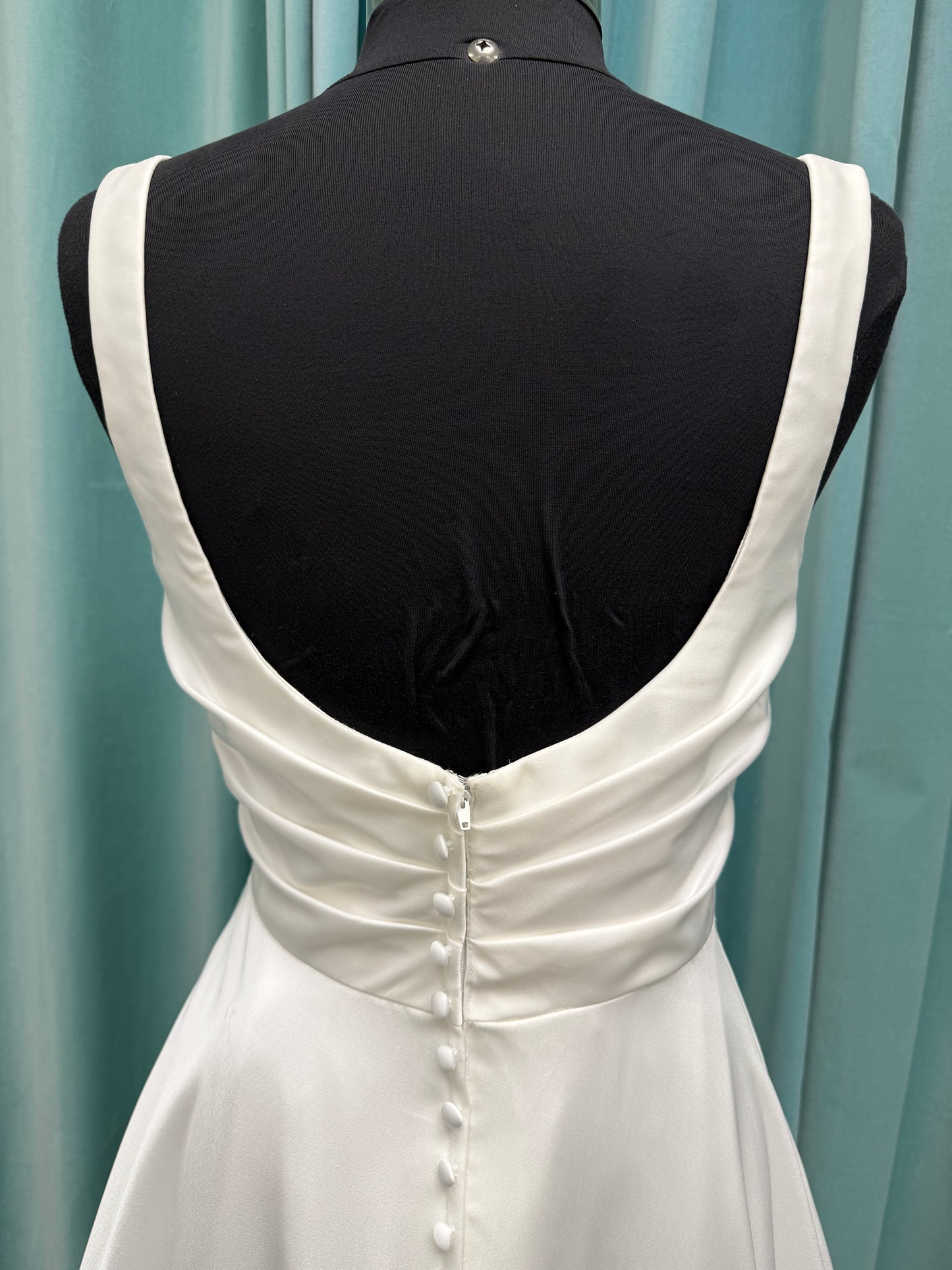 Stella York SY8110 ivory satin A-line wedding dress on mannequin with square neckline, shoulder straps, ruched bodice, and scoop back with fabric-covered buttons.
