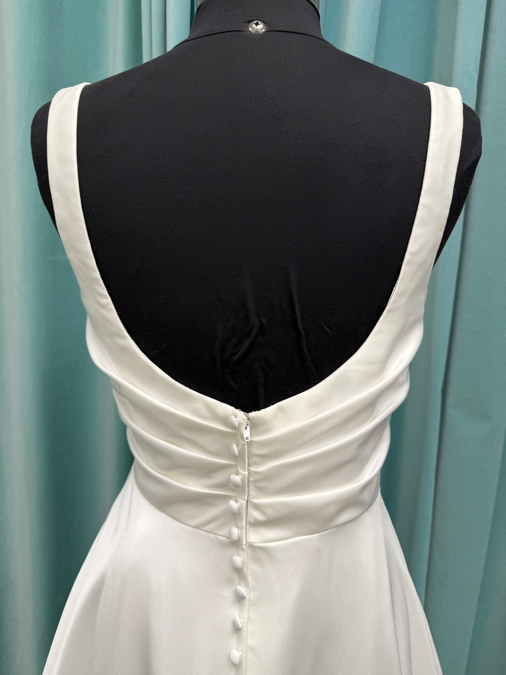 Stella York SY8110 ivory satin A-line wedding dress on mannequin with square neckline, shoulder straps, ruched bodice, and scoop back with fabric-covered buttons.

