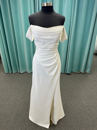 Tai ivory off-the-shoulder crepe sheath wedding dress on mannequin with draped bodice, front slit, and cathedral train.
