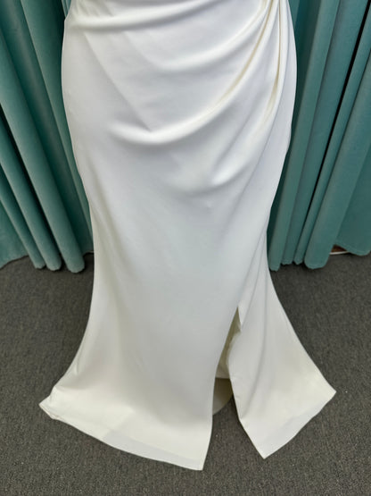 Tai ivory off-the-shoulder crepe sheath wedding dress on mannequin with draped bodice, front slit, and cathedral train.
