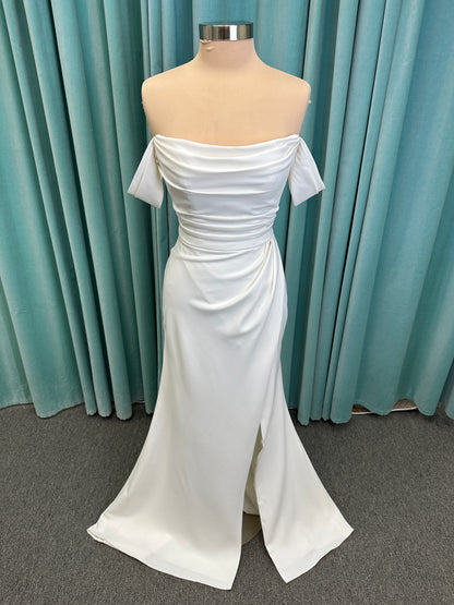 Tai ivory off-the-shoulder crepe sheath wedding dress on mannequin with draped bodice, front slit, and cathedral train.
