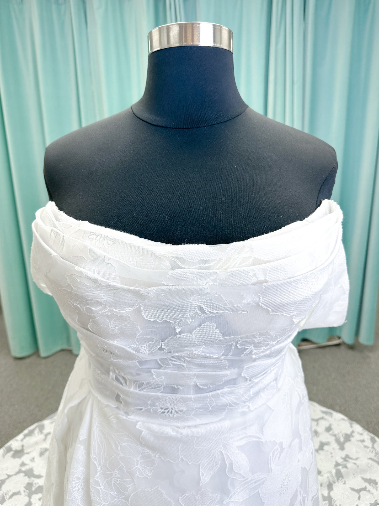 Willow ivory off-the-shoulder floral jacquard A-line wedding dress on mannequin with full skirt and front slit.
