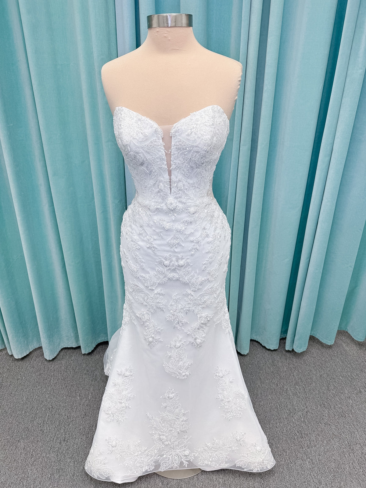 Moonlight Bridal J6996 Zira mermaid wedding dress on mannequin with strapless pointed sweetheart illusion neckline, side bodice cutouts, beaded lace appliques on shimmer net, drop waist, and chapel train with horsehair trim