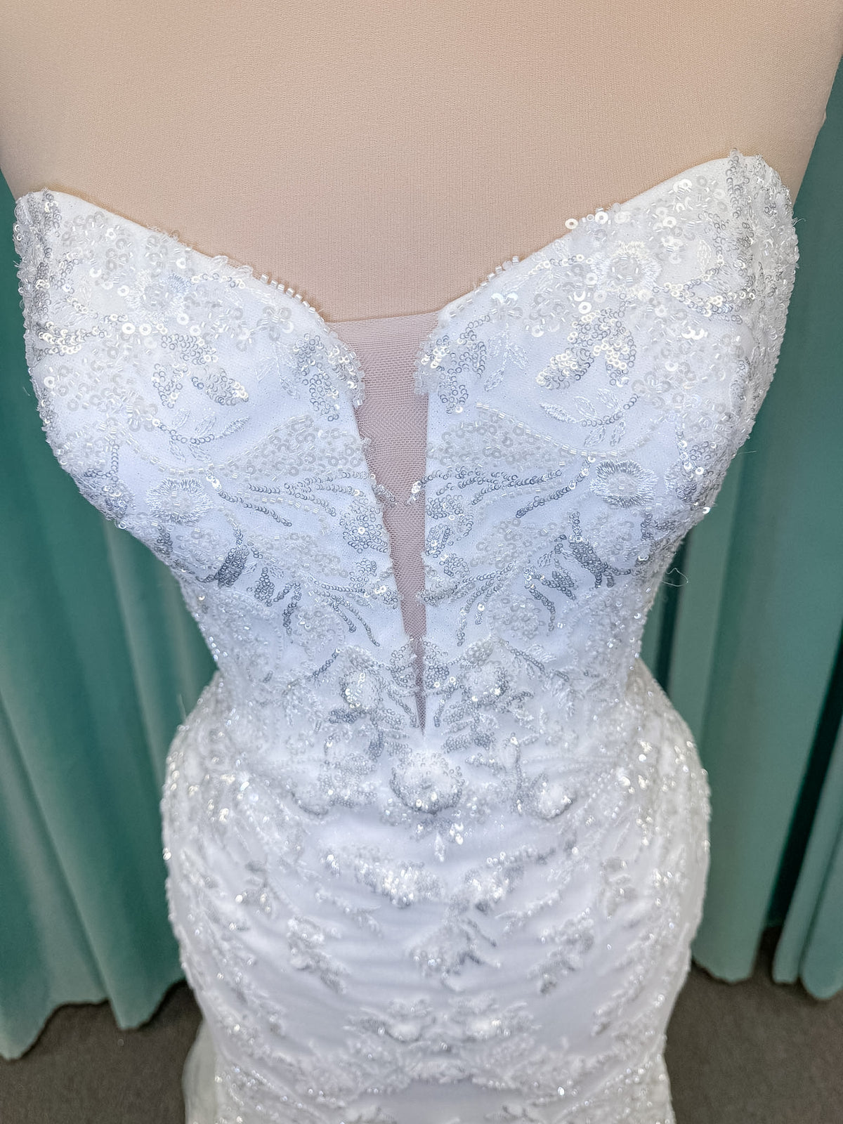 Moonlight Bridal J6996 Zira mermaid wedding dress on mannequin with strapless pointed sweetheart illusion neckline, side bodice cutouts, beaded lace appliques on shimmer net, drop waist, and chapel train with horsehair trim
