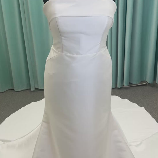 Oh Darling ivory strapless satin sheath wedding dress on mannequin with bandeau neckline, oversized statement bow at the waist, and voluminous overskirt.
