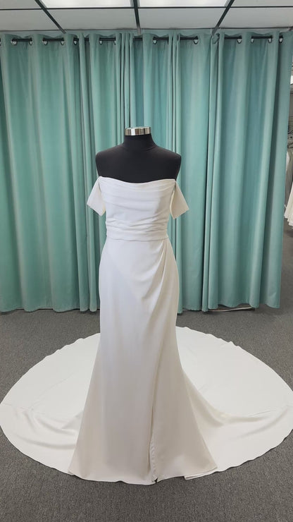 Tai ivory off-the-shoulder crepe sheath wedding dress on mannequin with draped bodice, front slit, and cathedral train.
