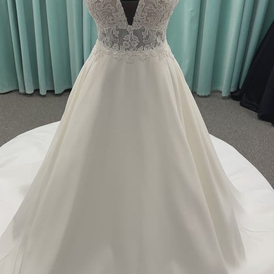 Satin A-line wedding dress with deep V-neckline, lace bodice, illusion tulle inset, and flowing skirt with pockets and long train