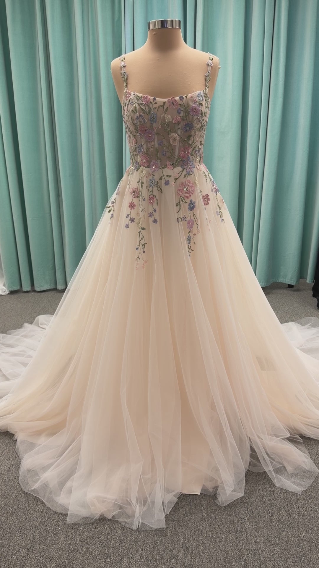 Stella York 8063 ivory and pastel colorful embroidered lace A-line wedding dress on mannequin with floral spaghetti straps, scoop neckline, and soft tulle skirt.

