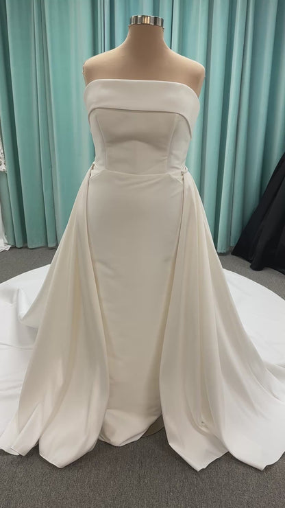 Oh Darling ivory strapless satin sheath wedding dress on mannequin with bandeau neckline, oversized statement bow at the waist, and voluminous overskirt.
