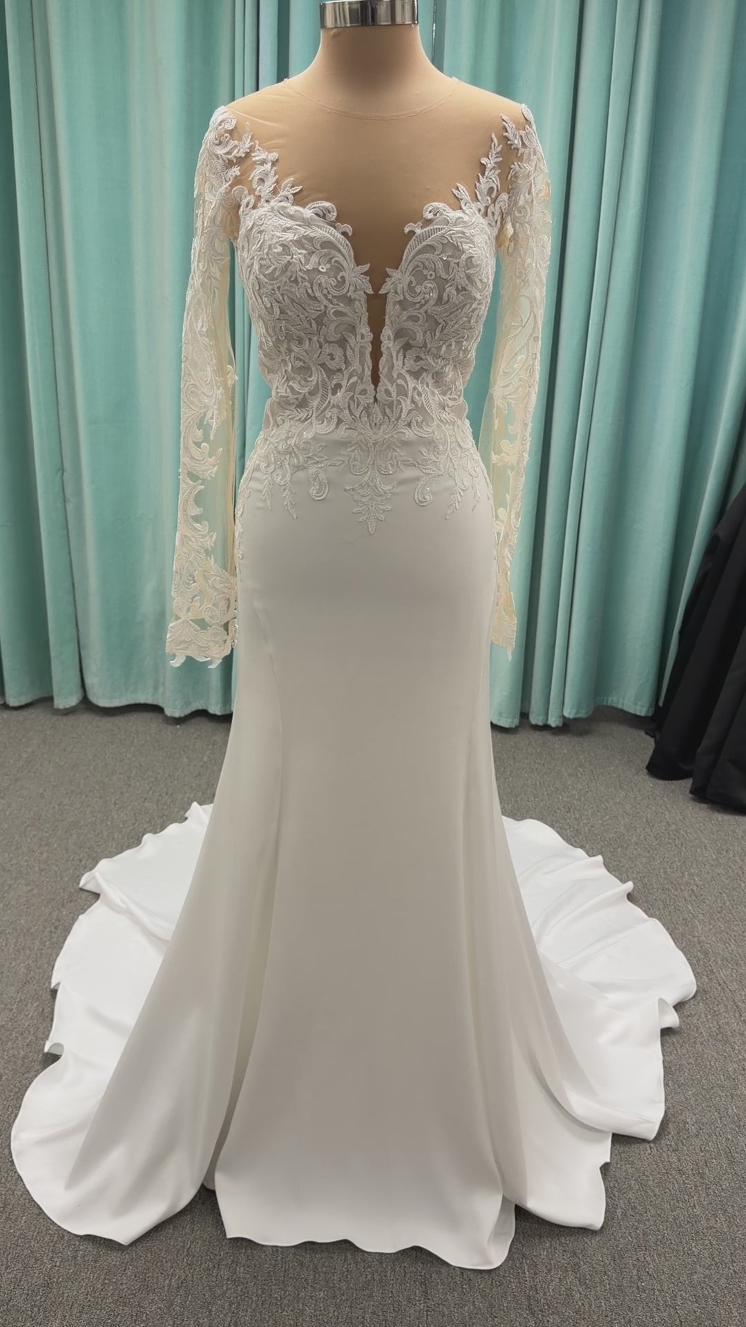 Stella York 8028 ivory lace fit-and-flare wedding dress on mannequin featuring high illusion neckline, sheer long lace sleeves, plunging bodice, and low open back.
