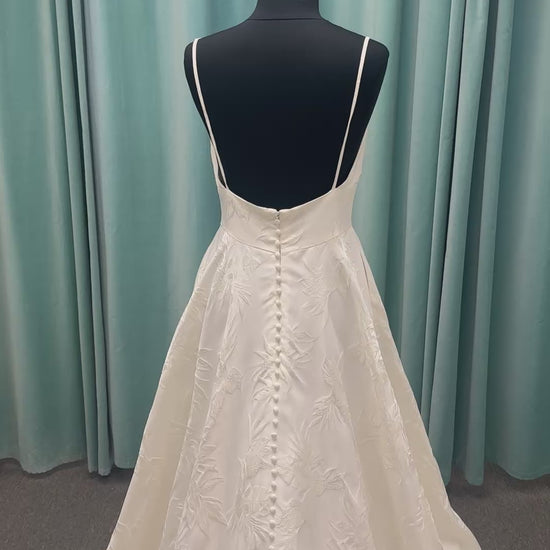 Lisha ivory spaghetti strap V-neck ballgown wedding dress on mannequin in floral jacquard fabric with a full sweeping skirt.
