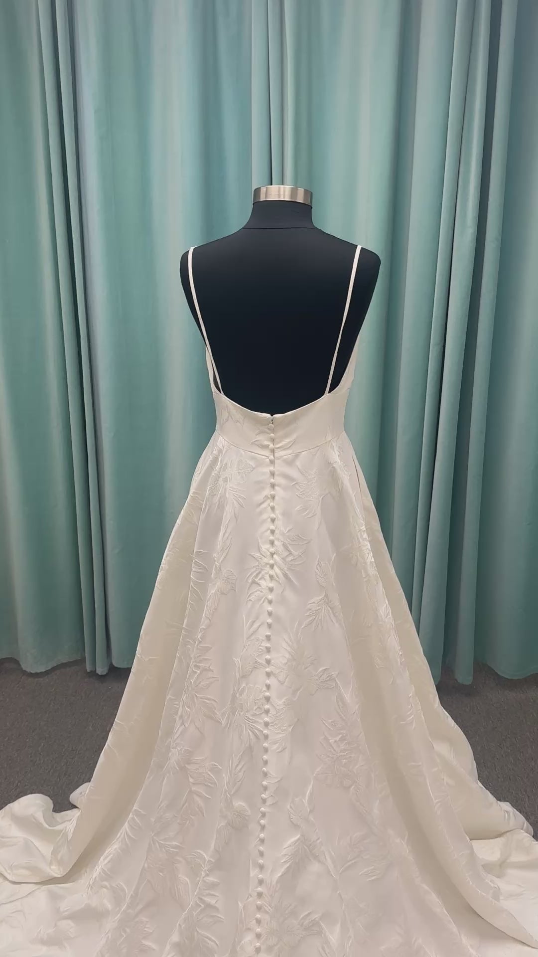 Lisha ivory spaghetti strap V-neck ballgown wedding dress on mannequin in floral jacquard fabric with a full sweeping skirt.

