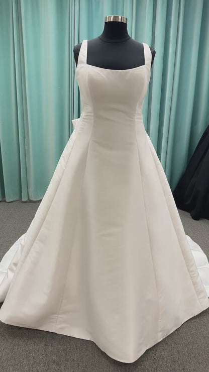 Minimalist Mikado A-line wedding dress with square neckline, clean seams, subtle side cutouts, and detachable oversized bow at the back