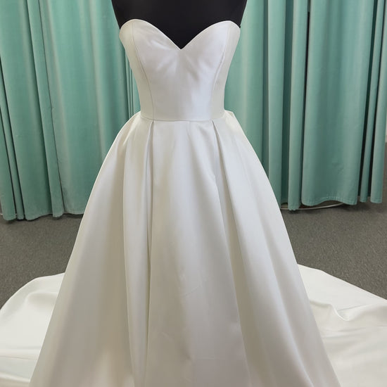 Achelios ivory strapless sweetheart satin ballgown wedding dress on mannequin with full skirt and clean structured bodice.
