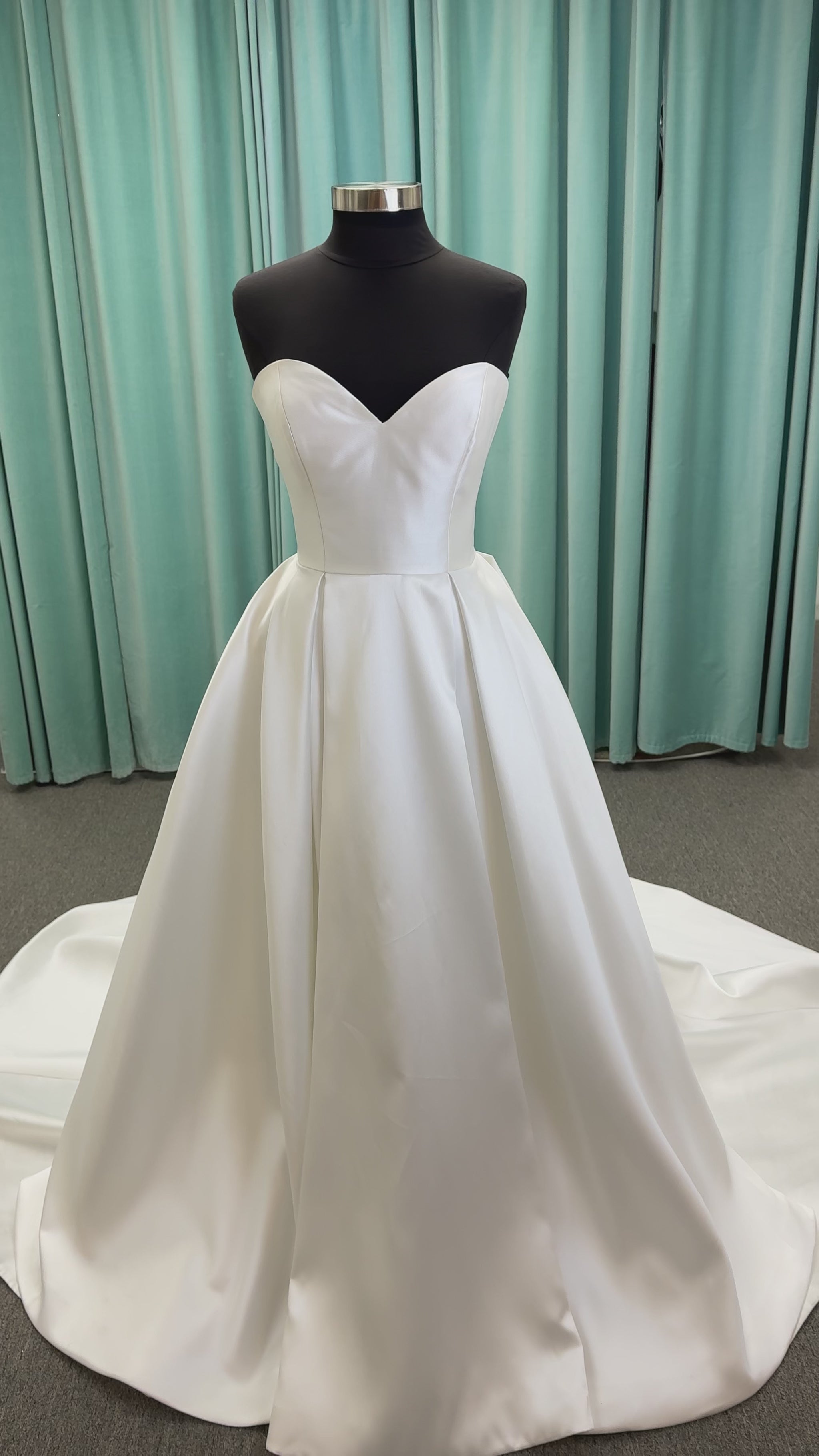 Achelios ivory strapless sweetheart satin ballgown wedding dress on mannequin with full skirt and clean structured bodice.
