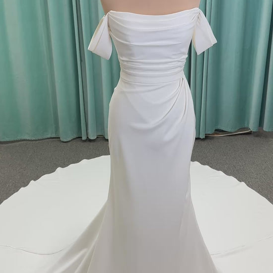 Tai ivory off-the-shoulder crepe sheath wedding dress on mannequin with draped bodice, front slit, and cathedral train.
